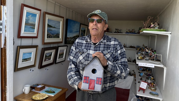 Alain Landry debout à l'entrée de sa galerie, tenant une cabane d'oiseau peinte à la main.