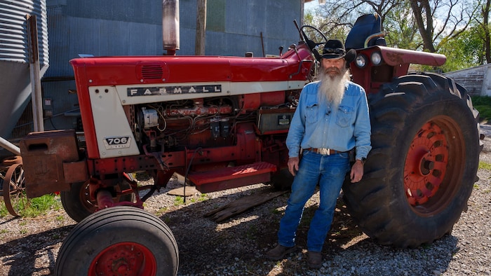 Un homme portant un chapeau de cowboy devant un tracteur sur une ferme.