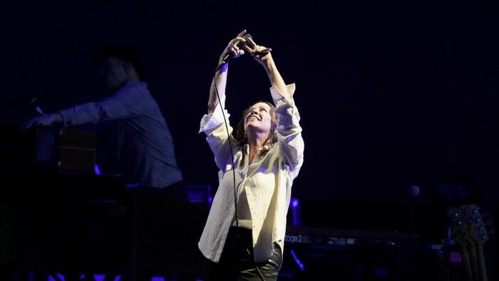 Alanis Morissette est sur scène, tient un micro, lève les deux bras et fait un arc au-dessus de sa tête tandis qu'elle regarde vers le haut.