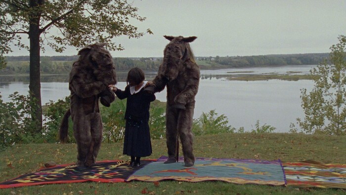 Une representation du movie When All the Leaves Are Gone montre une fille dehors avec deux personnes costumées en âne, à côté d'une étendue d'eau.