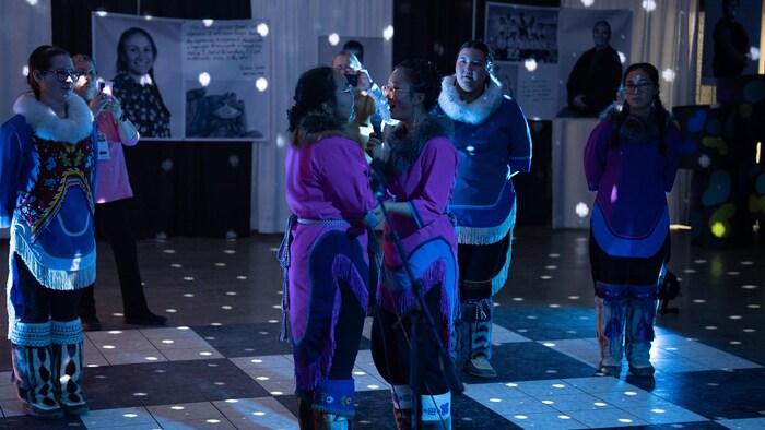 Deux jeunes femmes, qui se tiennent très près l'une en face de l'autre, font un chant de gorge lors du banquet culturel des Jeux d'hiver de l'Arctique en 2024. 