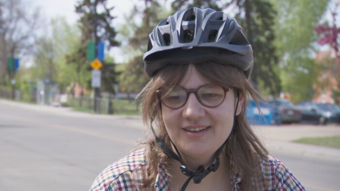 Une femme souriante portant un casque de vélo noir attaché sous le menton et des lunettes de vue, regarde légèrement vers le bas et la gauche au cours d'une entrevue.