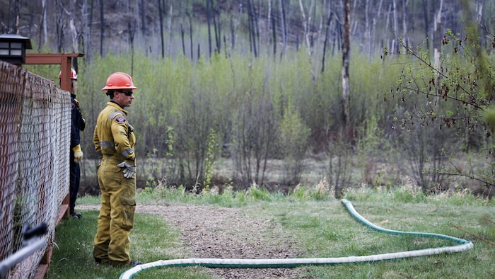 Des pompiers surveillent un tuyau d'arrosage pour incendies de forêt dans le quartier évacué de Grayling Terrace à Fort McMurray, en Alberta, le jeudi 16 mai 2024.