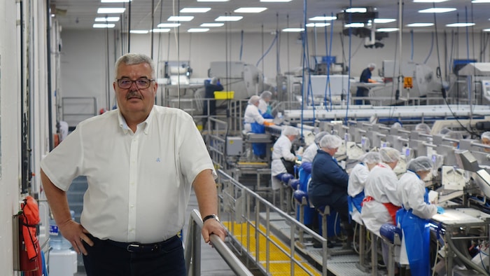 Alberto Wareham pose dans une usine, devant une dizaine d'employés qui travaillent devant un comptoir.