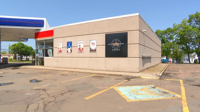 Une enseigne portant le logo d'Alcool NB et le mot « agent » sur la façade d'un dépanneur attenant à une station-service.