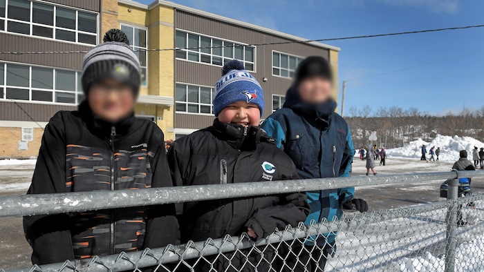 Trois jeunes garçons dans une cour d'école en hiver.