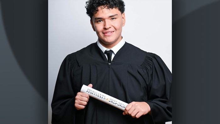 Un jeune homme avec une toge de finissant qui tient un diplôme.