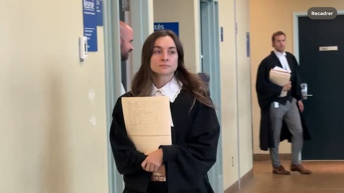L'avocate portant la toge tient des documents dans ses mains à l'extérieur de la salle d'audience.