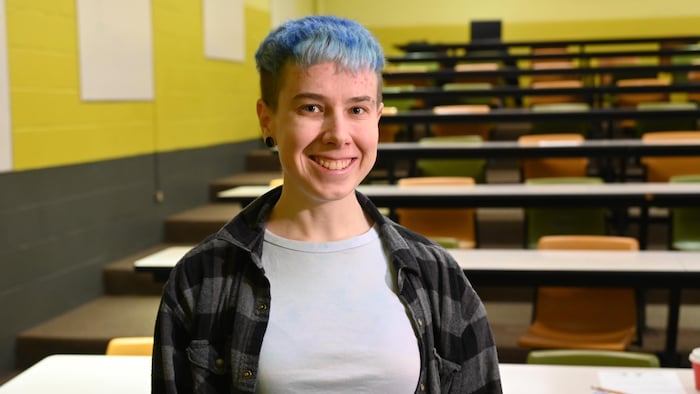 Une personne aux cheveux bleus portant une chemise noire et grise.