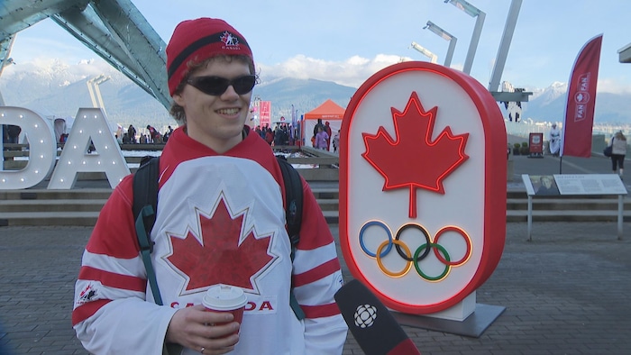 Alex Biedka porte un café à la main et est vêtu d'un maillot de hockey où il est écrit Canada