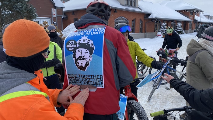 Un homme colle sur le dos d'un autre homme une affiche qui présente le rassemblement du 31 janvier. 