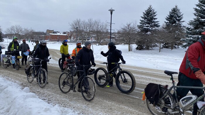 Des cyclistes marchent à côté de leur vélo dans une rue enneigée.