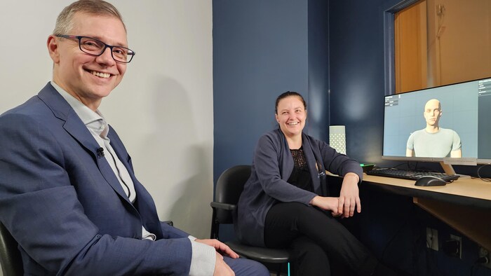 Deux personnes sont assises devant un écran qui montre l'avatar d'une personne.