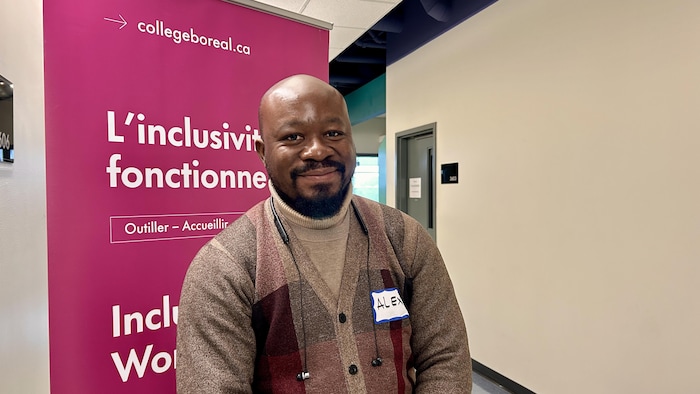 Alexandre Pondy, souriant, pose devant une banderole rétractable du Collège Boréal qui porte sur l'inclusivité.