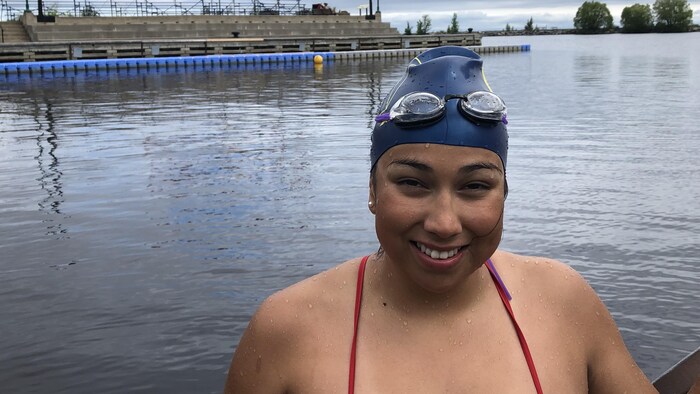 Avec son bonnet de natation sur la tête, Alexann Petiquay sourit à proximité d'un plan d'eau.