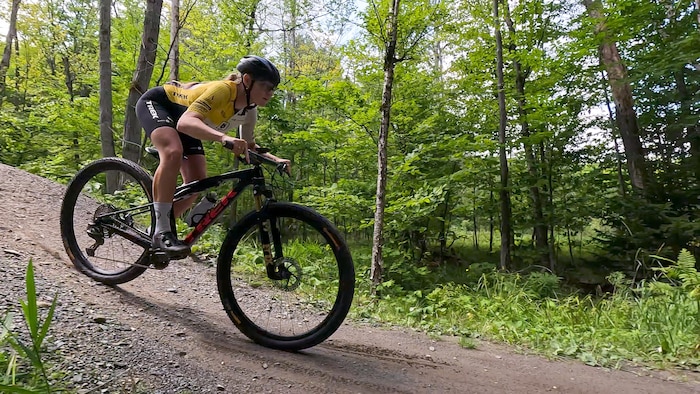 Elle descend une pente, penchée vers l'avant sur son vélo.
