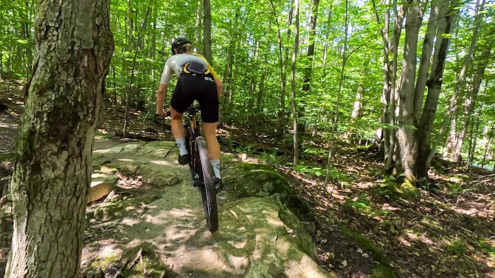 Alexia Harel roule sur une grosse roche dans un sentier de vélo de montagne.