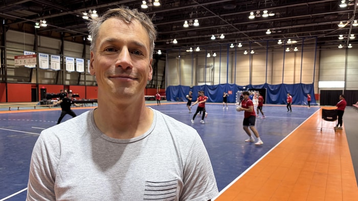 Il pose pour une photo devant un terrain de handball.