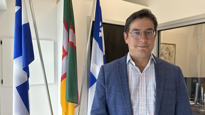 Alexis Brunelle-Duceppe devant des drapeaux, à l'intérieur de son bureau.