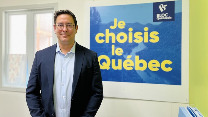 Un homme devant une pancarte du Bloc québécois.