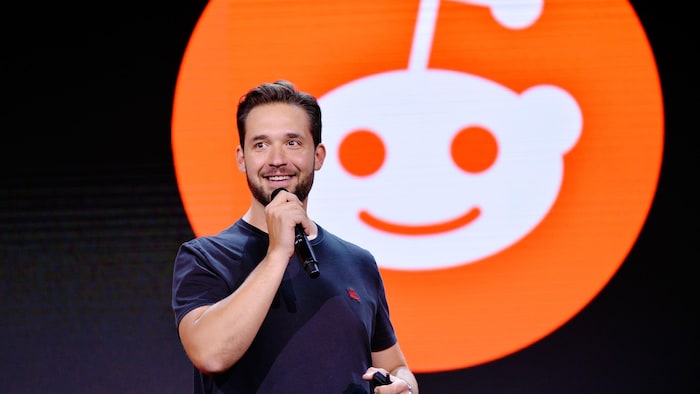 Un homme parle dans un micro devant le logo du réseau social Reddit. 