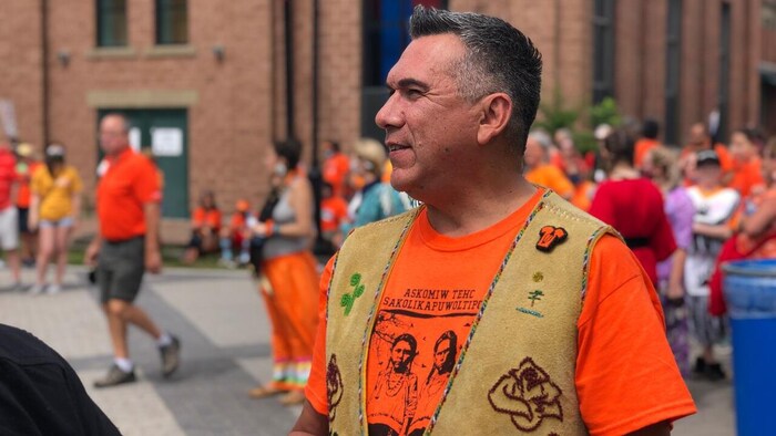 Allan Polchies de profil, sur une place publique, vêtu d'un vêtement orange.