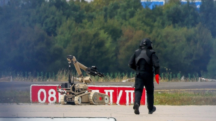 Un agent de police en tenue de protection marche à côté d’un robot de neutralisation d’explosifs à l’aéroport de Leipzig.