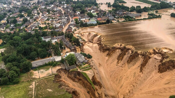Vue aérienne d'un énorme cratère qui s'est formé à proximité d'un village, dans lequel se déversent des trombes d'eau.