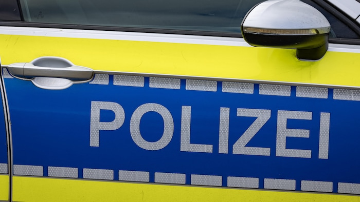 La portière latérale d'une voiture de police jaune et bleue affiche l'inscription « POLIZEI » en lettres majuscules réfléchissantes. Le visuel montre également le rétroviseur et la poignée argentée du véhicule.