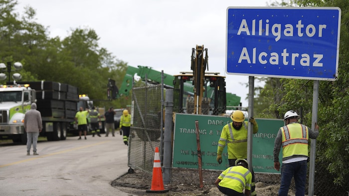 Des travailleurs installent un panneau indiquant « Alligator Alcatraz », à l'entrée de l'aéroport en Floride.