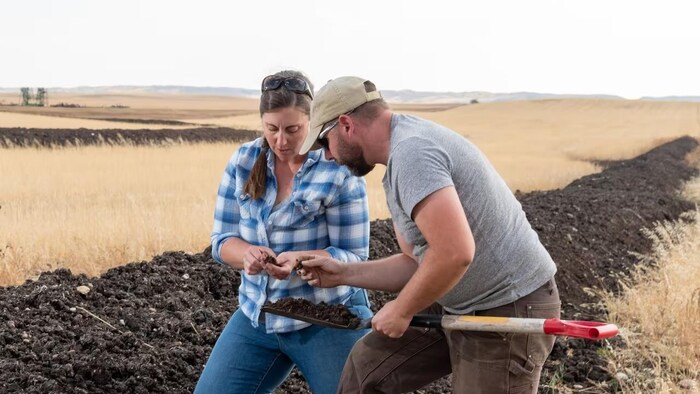 A woman and a man looking at a soil sample in a field.