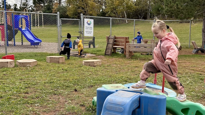Allorah Gaudet marche sur un parcours d'obstacles dans la cour de récréation du CPE Le Jardin des Étoiles. Au fond, d'autres enfants courent et jouent. 