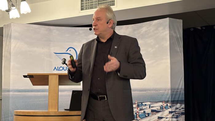 Un homme en complet, portant un micro, parle.