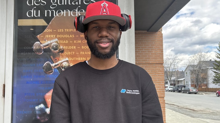 Une casquette rouge sur la tête un jeune homme est adossé et sourit à la caméra