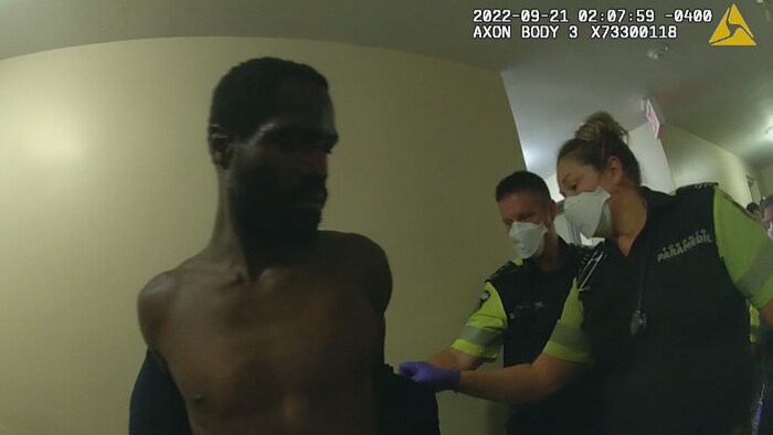 Un homme, torse nu, dans un corridor d'immeuble à appartements.