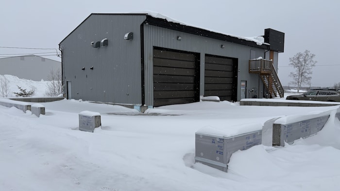 L'extérieur d'une petite usine avec deux grandes portes de garage, sur un sol enneigé.