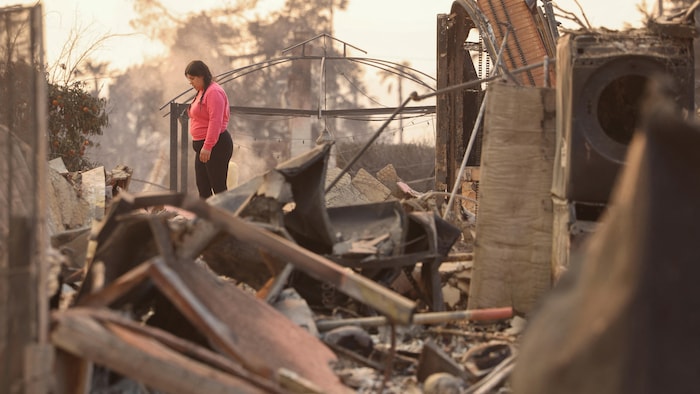 Une femme, debout au milieu des ruines, regarde vers le sol.