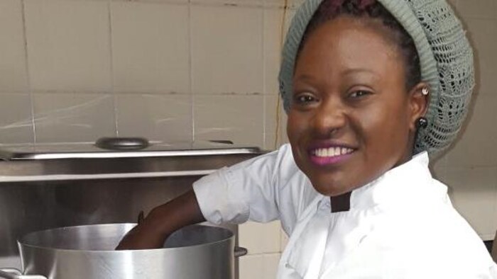 Ama Akofa, en tenue de cheffe cuisinière, plonge la main dans un chaudron en acier inoxydable.