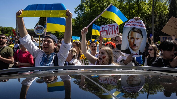 Des personnes brandissant les couleurs ukrainiennes entourent une voiture en criant des slogans. 