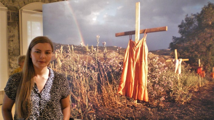 Mains dans les poches, une jeune femme pose devant une photo en grand format dans une exposition.