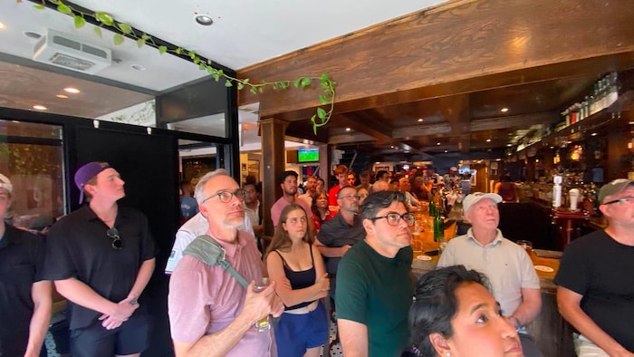 Des gens dans un bar regardent une télé.