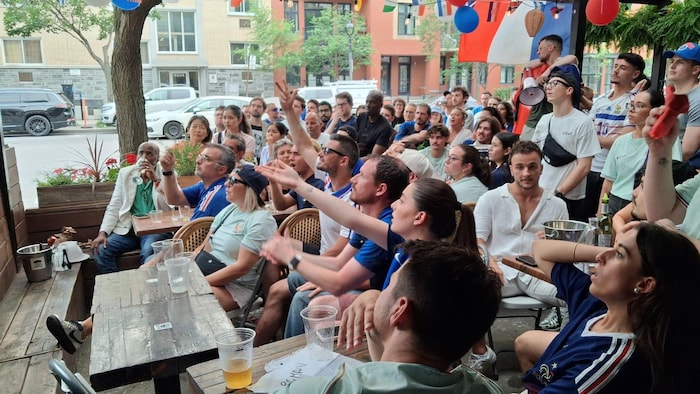 Une foule regarde un match de soccer sur une terrasse.
