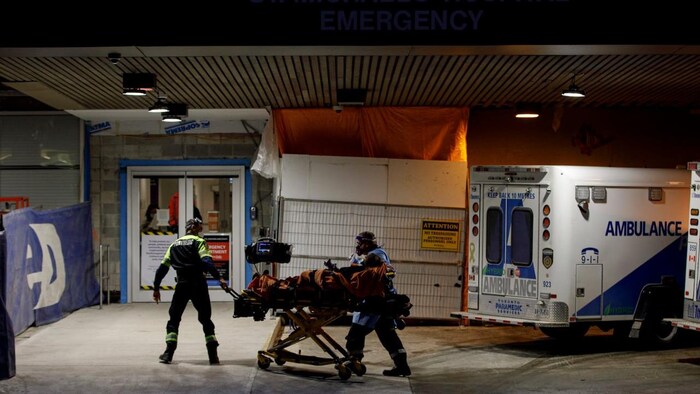 Two paramedics bringing a person on a gurney to the emergency room of a hospital.