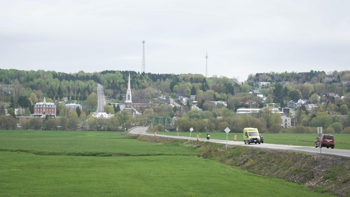 Une ambulance sur la route d'un village avec au loin, un pont et une église.
