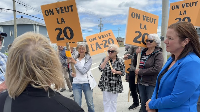 La députée Amélie Dionne discute avec des manifestants. Ils ont en main des pancartes réclamant le prolongement de l'autoroute 20.