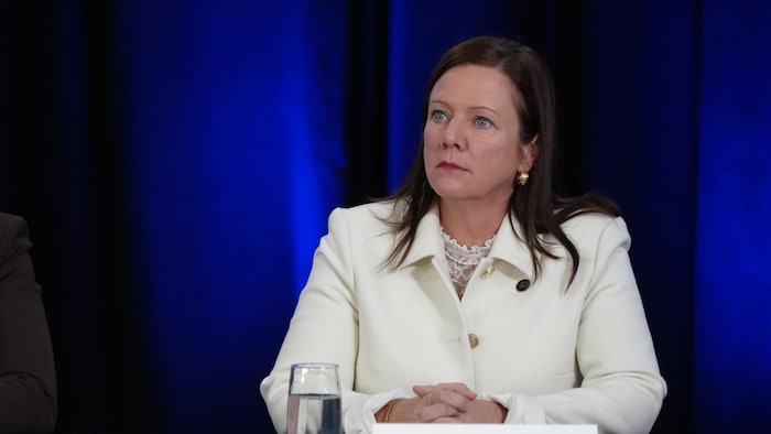 Amélie Dionne est assise à la table de la conférence de presse et écoute les allocutions.
