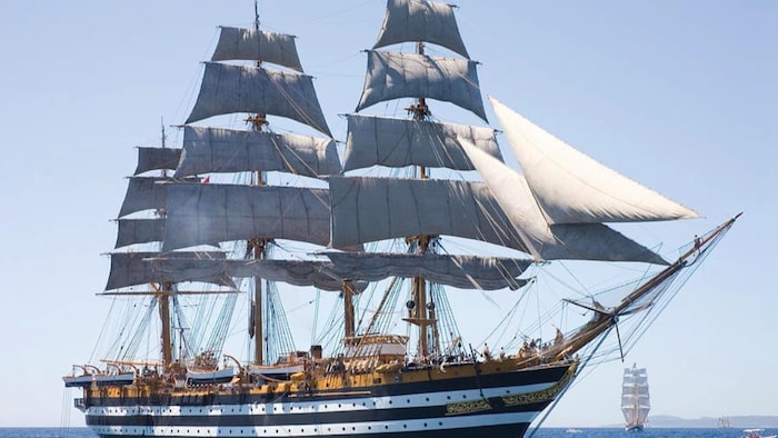Le grand voilier italien Amerigo Vespucci naviguant en mer, toutes voiles déployées sur ses trois mâts, avec sa coque caractéristique rayée de noir et de blanc.