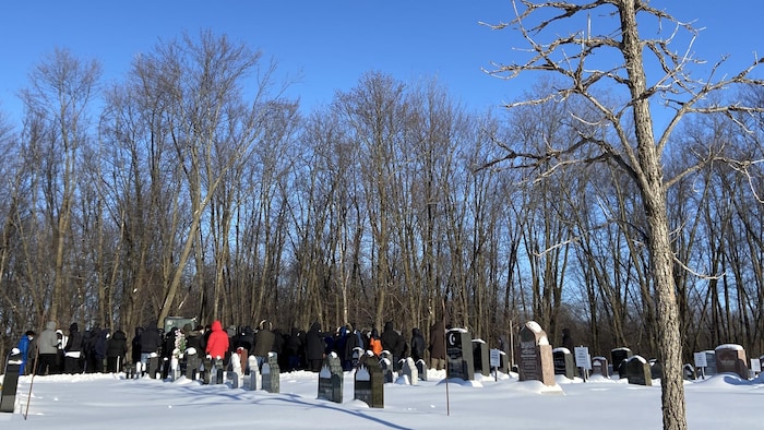 Des personnes debout dans un cimetière avec des tombes recouvertes de neige.