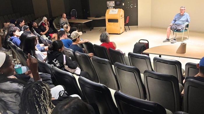 Des jeunes assis dans un auditorium écoutent avec attention la présentation d'un homme amputé d'une jambe.