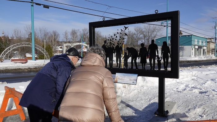 Deux personnes regardent la structure commémorative d'Amqui.